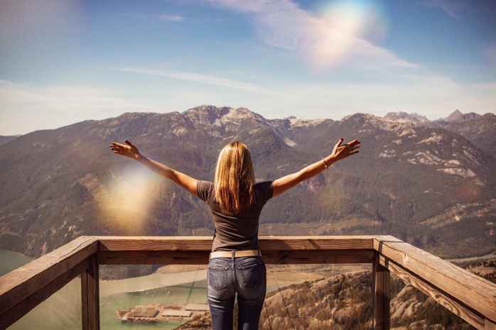 woman facing mountains raising her hands