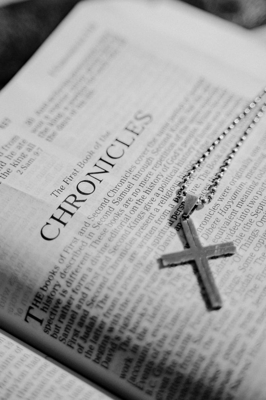grayscale photo of a holy bible with a cross pendant